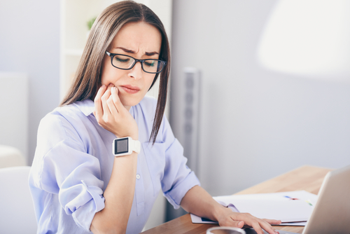 Woman in her office holding her jaw in pain caused by dental emergency